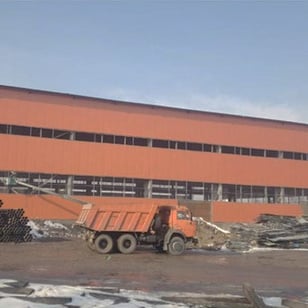 Производственное здание: длинный корпус из оранжевых сэндвич-панелей и самосвал на площадке