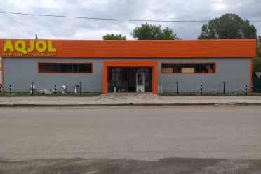 Одноэтажное здание с вывеской «AQJOL Qurylys tauarlary»: серые стеновые панели и оранжевый фриз
