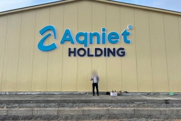Стена здания из бежевых стеновых сэндвич-панелей с вывеской «Aqniet Holding»