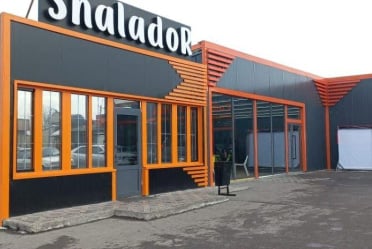 Фасад здания с вывеской «Shalador»: графитовые панели, оранжевые рамы окон и декоративные ламели